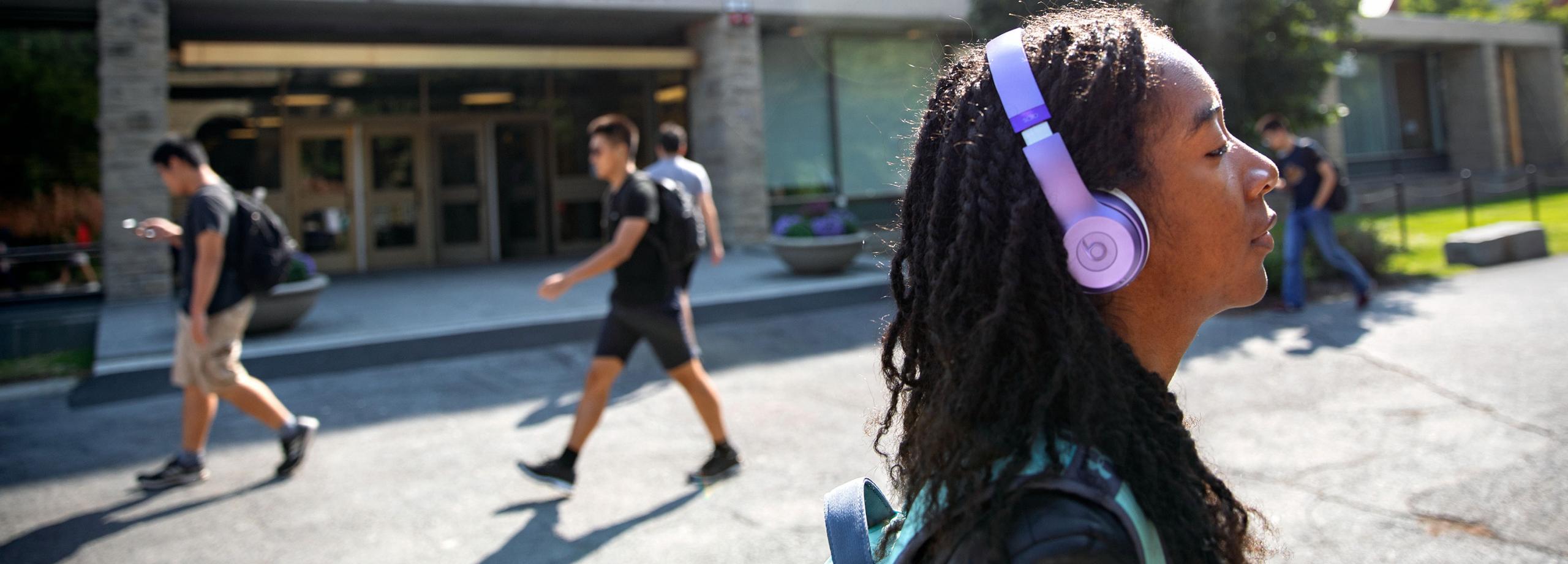 Student walking through campus with headphones on